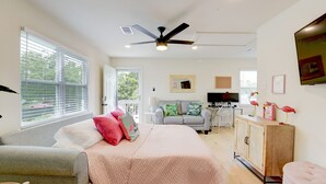 A bedroom with a bed, a grey sofa, a wooden cabinet, a ceiling fan, and a TV.