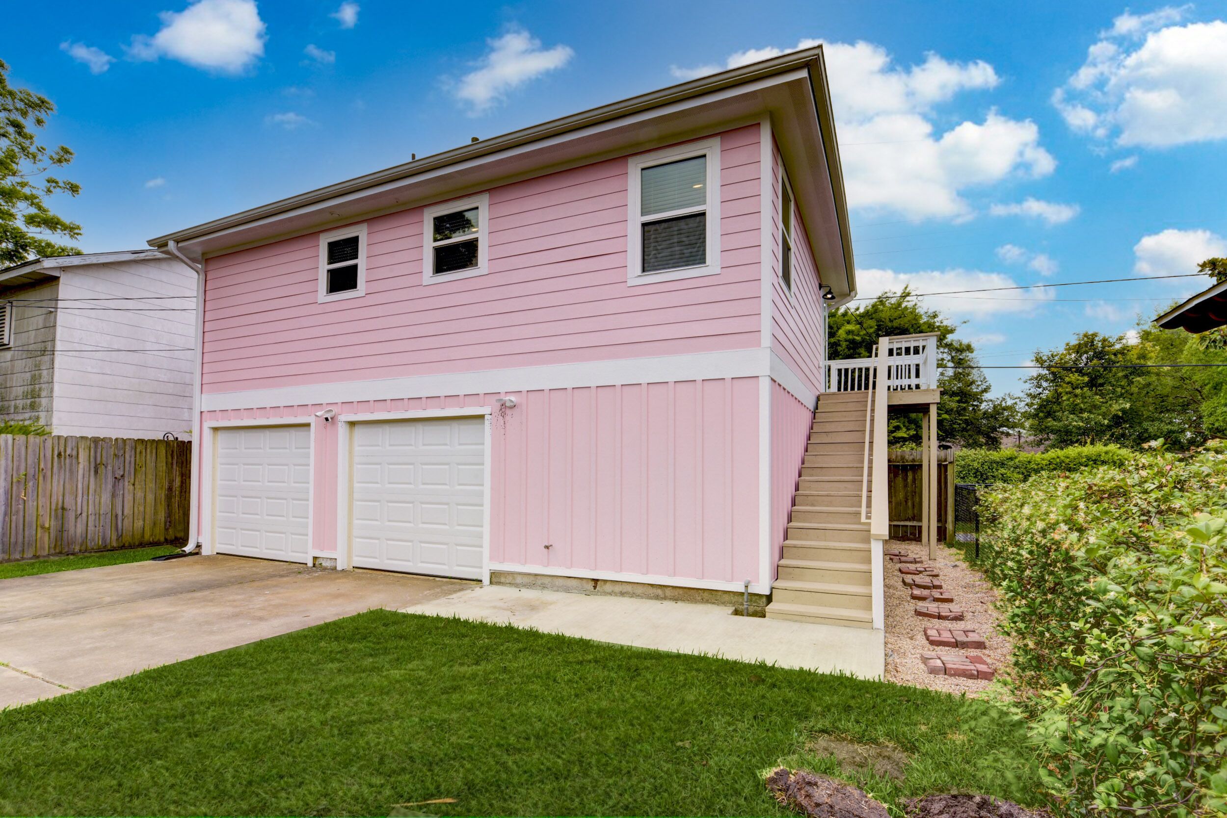 Uma casa de dois andares com fachada rosa, duas portas de garagem e um pequeno alpendre.