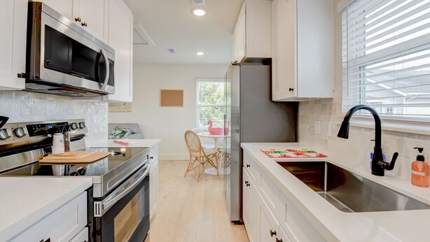 A modern kitchen with white cabinetry, stainless steel appliances, and a window with blinds.