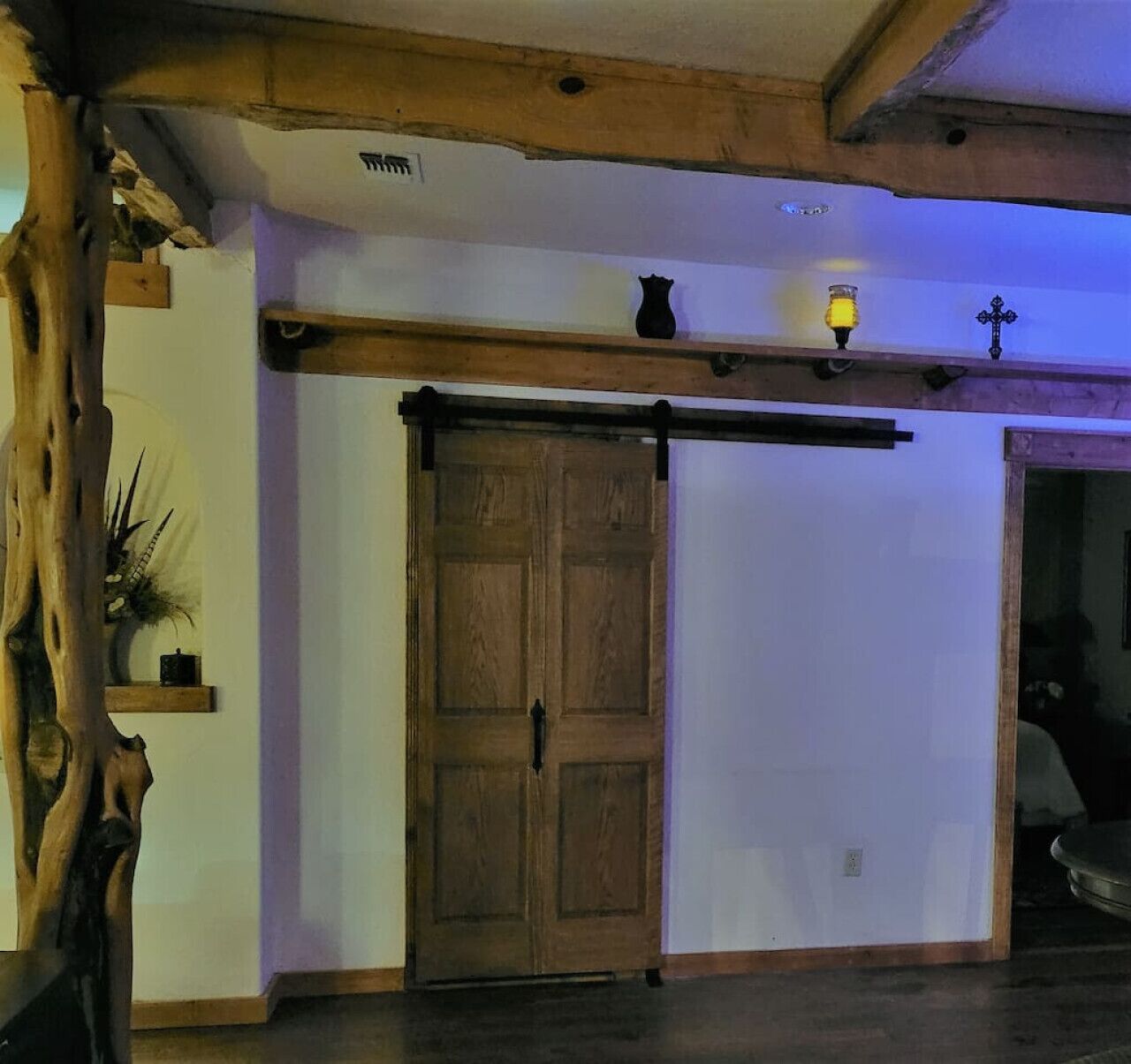 Een kamer met een houten deur, een klein plankje met een bloempot en een wandlamp.