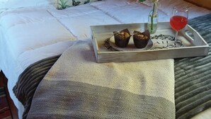 A neatly made bed with white linens, a floral pillow, a tray with muffins and a glass of red drink, and a decorative vase with flowers. - Comfy cabin for two close to Grand Canyon and many Northern Arizona attractions (Williams)