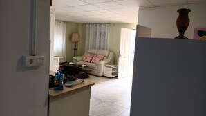A living room with a sofa, a coffee table, and a lamp. There is a kitchen area with a stove and a sink. - Bella Vista Apartment (Coin)