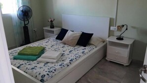 A bedroom with a bed, nightstands, a fan, and a bedside lamp. - Bella Vista Apartment (Coin)