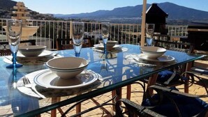 A dining table set for four with clear glassware and plates, overlooking a mountainous landscape. - Bella Vista Apartment (Coin)