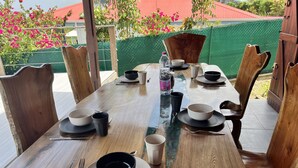 Une table à manger dressée avec des assiettes, des bols, des tasses et des couverts, entourée de chaises en bois.