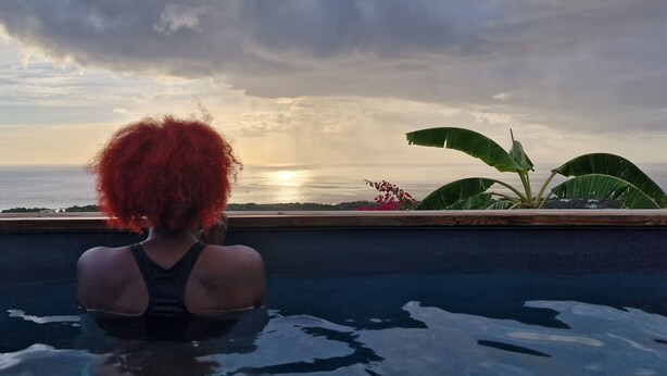 Une personne dans une piscine avec vue sur l’océan et un coucher de soleil.