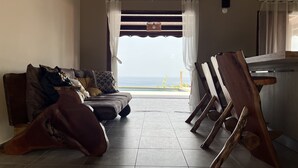 Une pièce avec vue sur la mer, un canapé avec des coussins, une chaise en bois et une table.