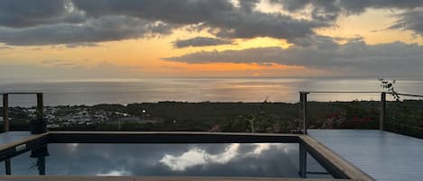 A rooftop pool with a view of the sea and a sunset.