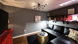 Un salon avec un canapé en cuir noir, un meuble rouge, une table ronde dorée et un luminaire au plafond.