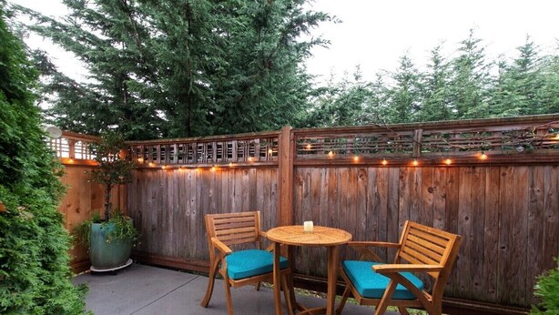 Une terrasse en bois avec deux chaises en bois et une petite table ronde, entourée d’une clôture en bois et illuminée de guirlandes lumineuses.