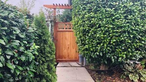 Une porte en bois qui mène à un jardin agrémenté d’une pergola et de diverses plantes.