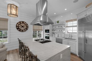 A modern kitchen with a central island, stainless steel appliances, and a large wall clock.