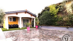 A house with a covered patio area, a small seating area with chairs, and potted plants. - Le Rivat - COMMUNAY - Gîte (COMMUNAY)