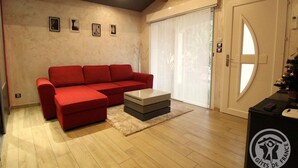 A living room with a red sofa, a coffee table, and a door with a frosted glass window. - Le Rivat - COMMUNAY - Gîte (COMMUNAY)