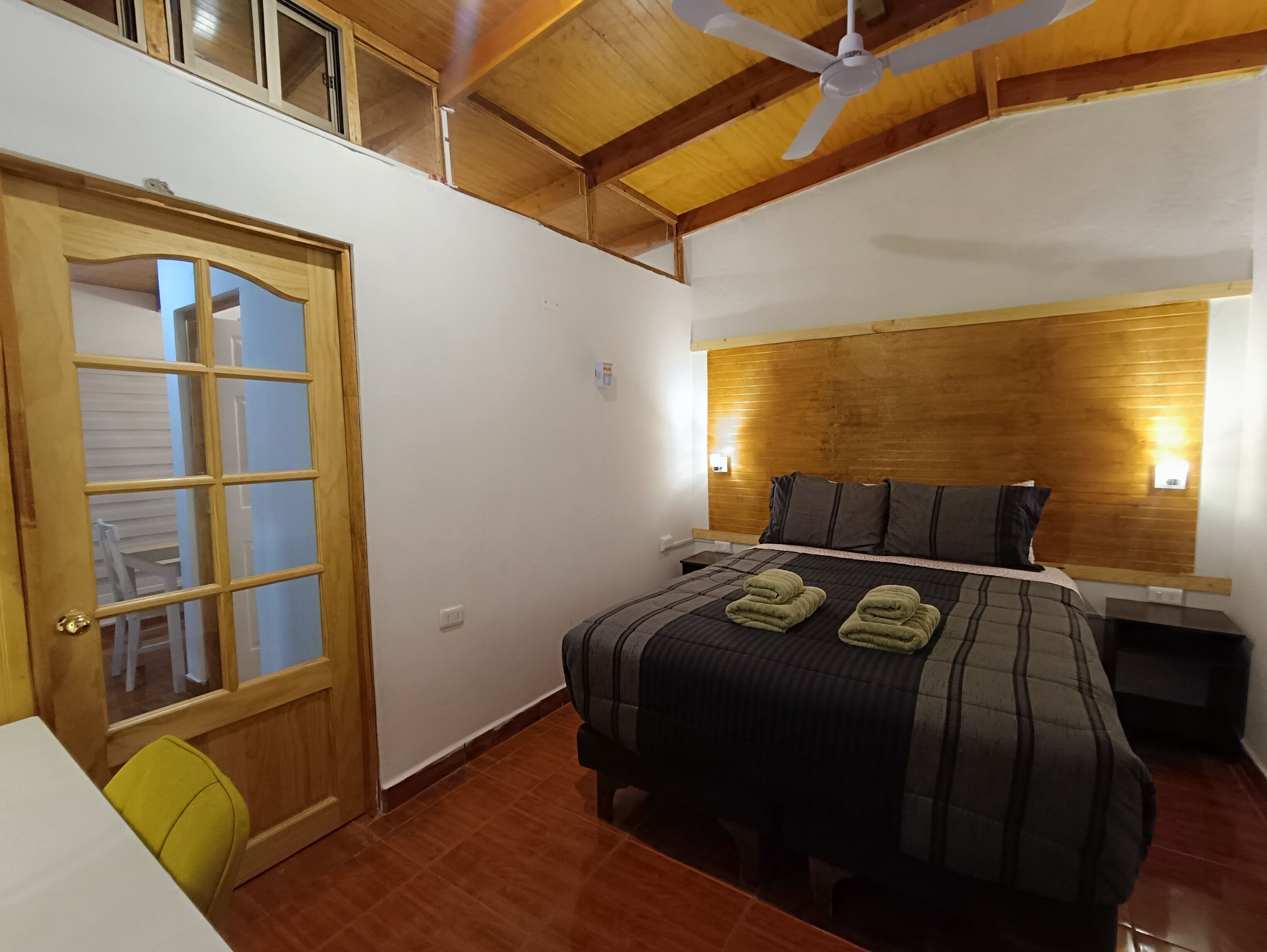 A bedroom with a wooden headboard, a bed with a plaid bedspread, and two green towels on the bed.