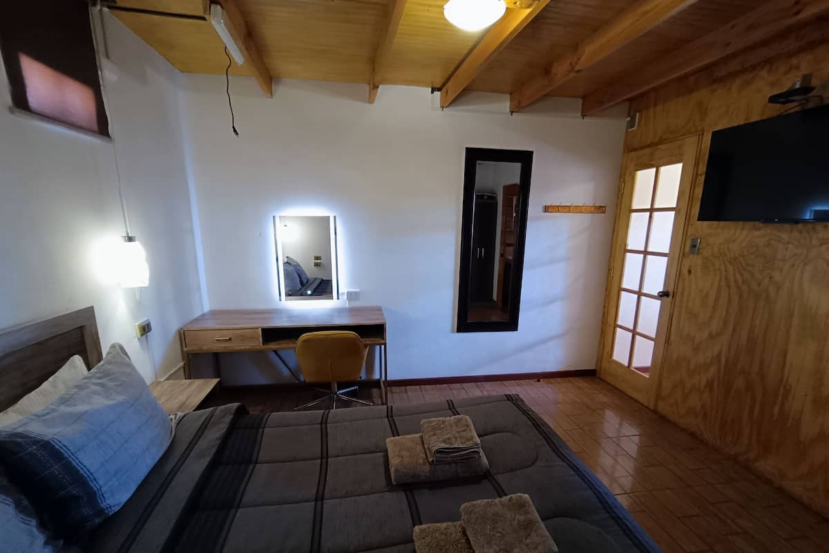 A room with a bed, a desk, a chair, a mirror, and a window.
