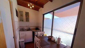 A compact kitchen with white cabinets, a wooden table, and a large window. - Yurak Apart Hotel (San Pedro de Atacama)