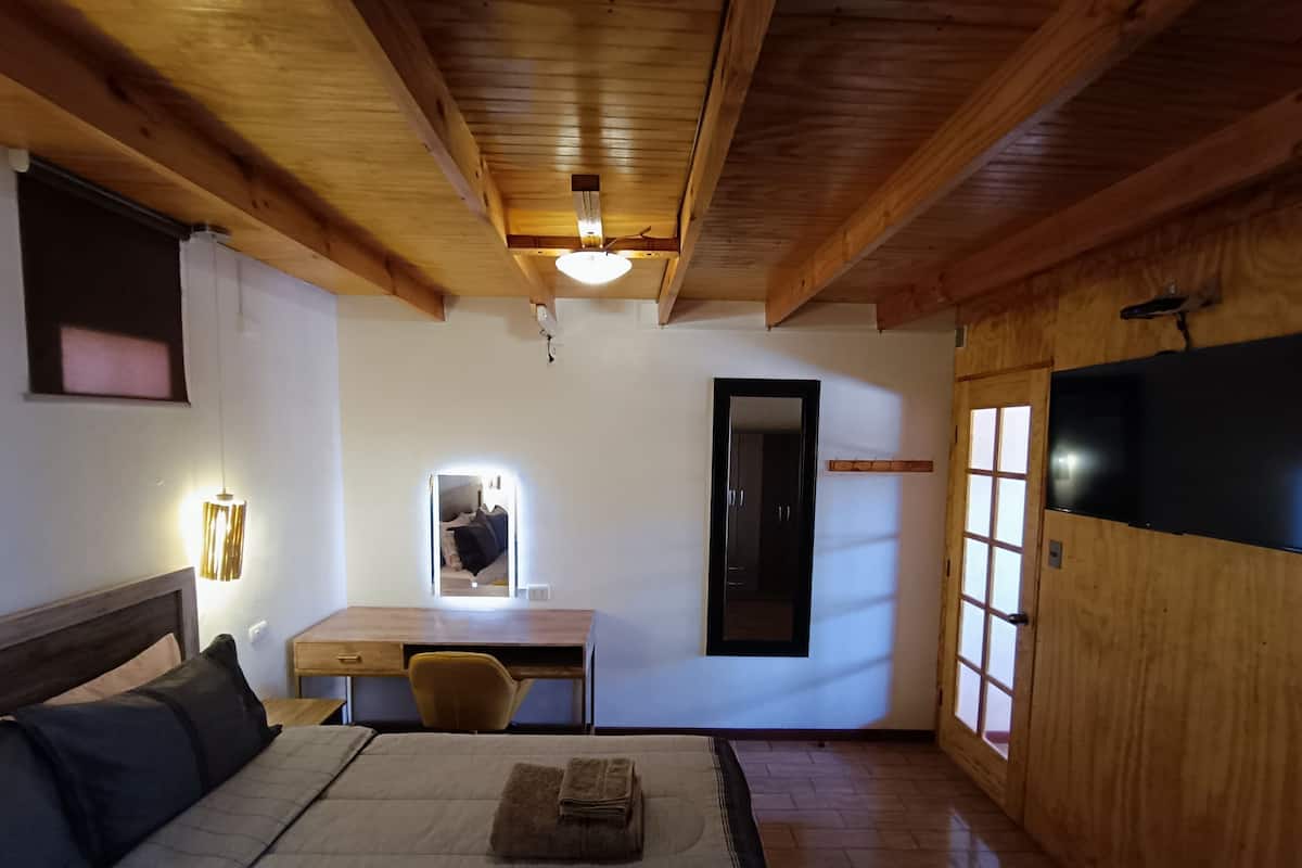 A room with a bed, a desk, a chair, a mirror, and a TV.