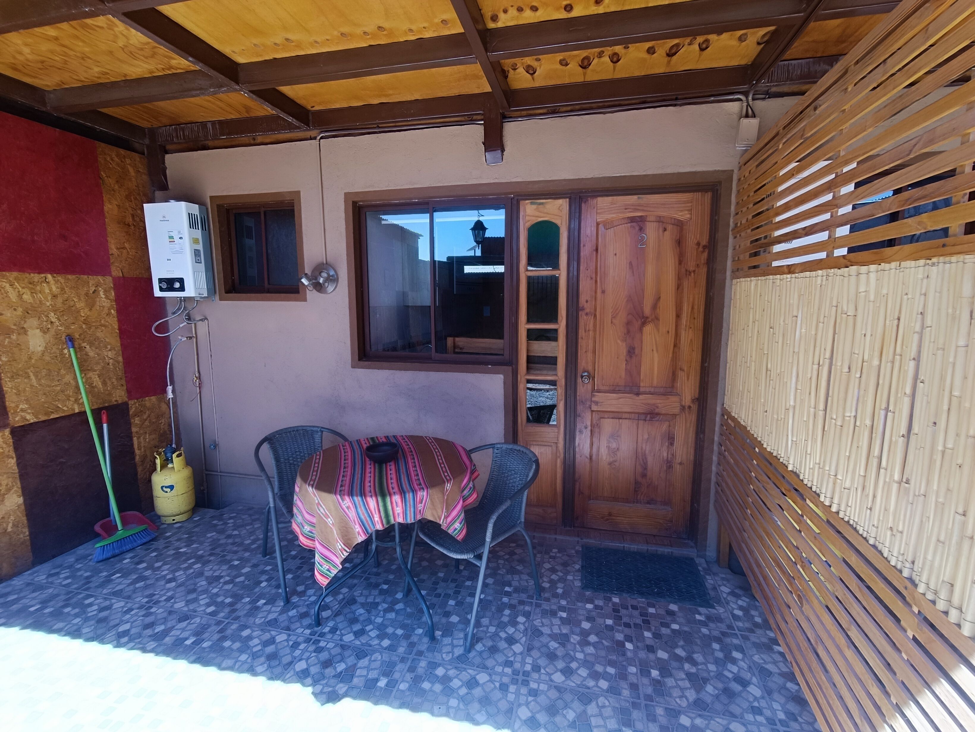 A small patio area with a table and chairs, a wooden door, and a window.