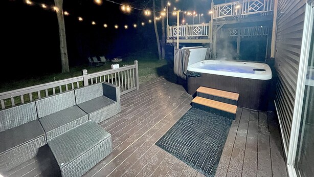 Ein Whirlpool auf einer Holzterrasse mit Lichterketten, einem überdachten Sitzbereich und Blick auf das Haus.
