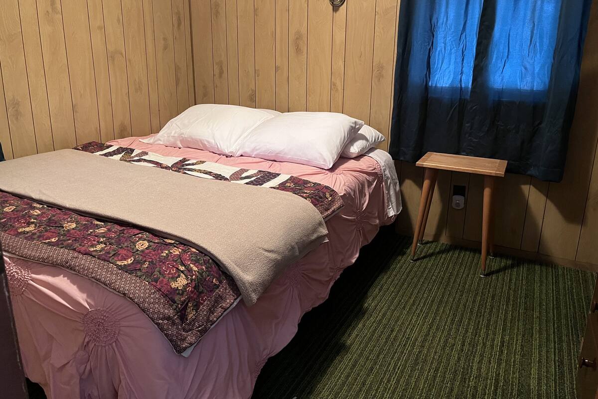 Ein Bett mit floralem Überwurf, einem Holzkopfteil und einem Nachttisch mit Lampe.