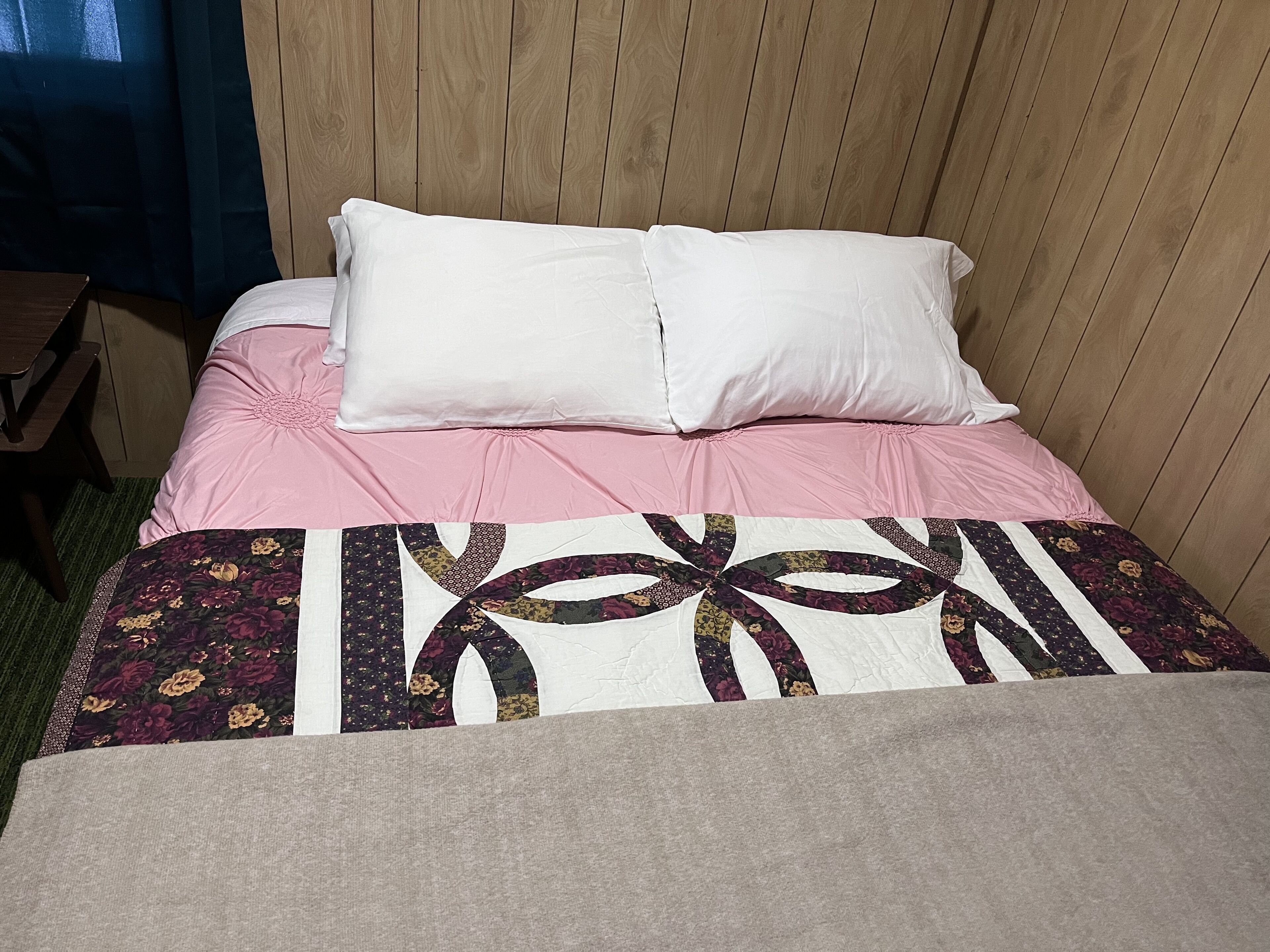 A bed with a pink bedspread, white pillows, and a quilt with floral patterns.
