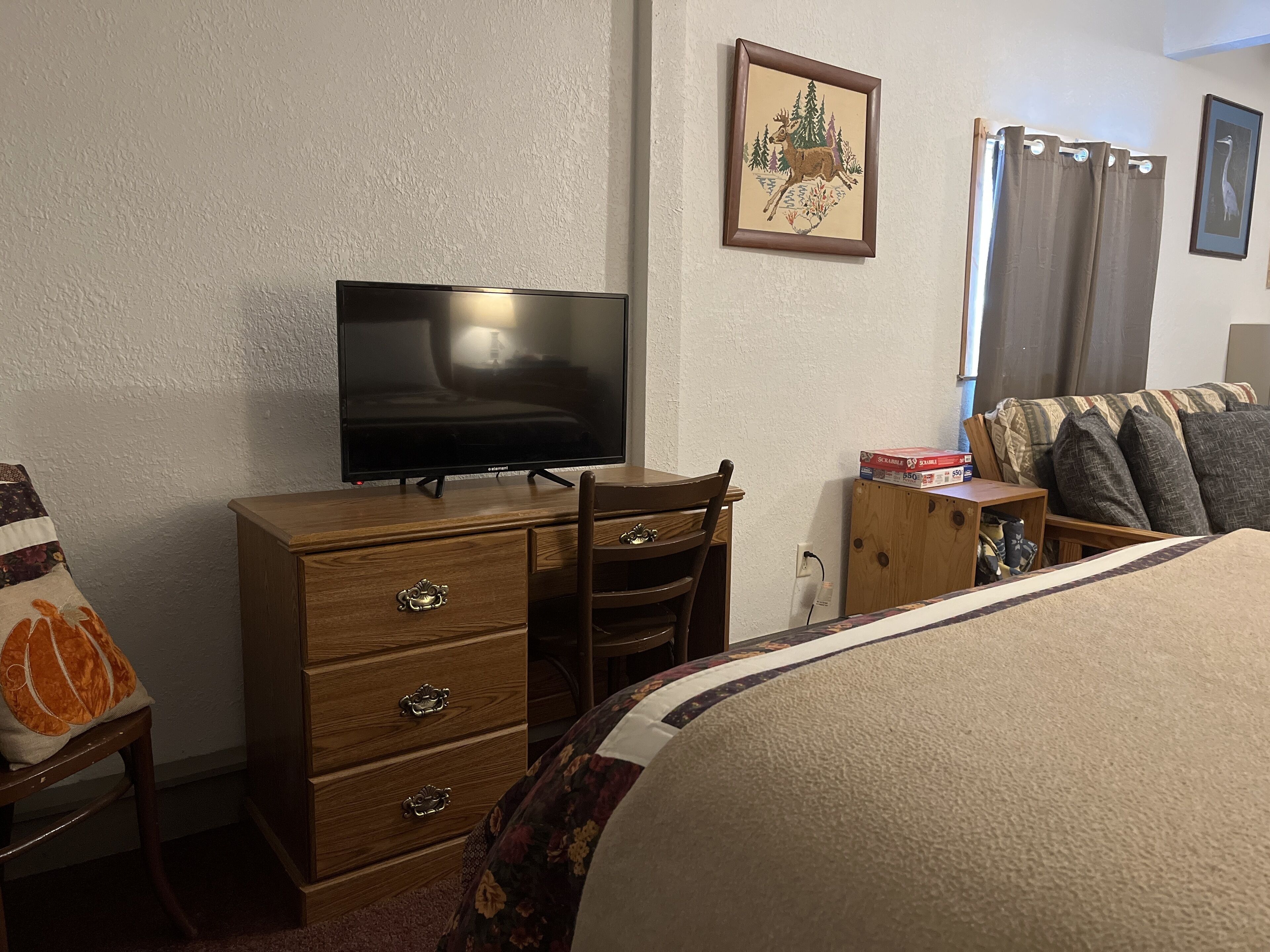 Una habitación de hotel con una cama, un aparador de madera con cajones, un televisor sobre el aparador, una mesita de madera con una caja de pizza, y un cuadro colgado en la pared.