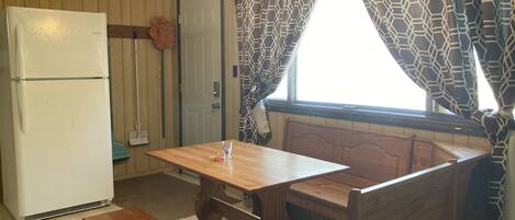 Une cuisine de taille réduite, avec une table et un banc en bois, un réfrigérateur blanc et des rideaux à motifs.