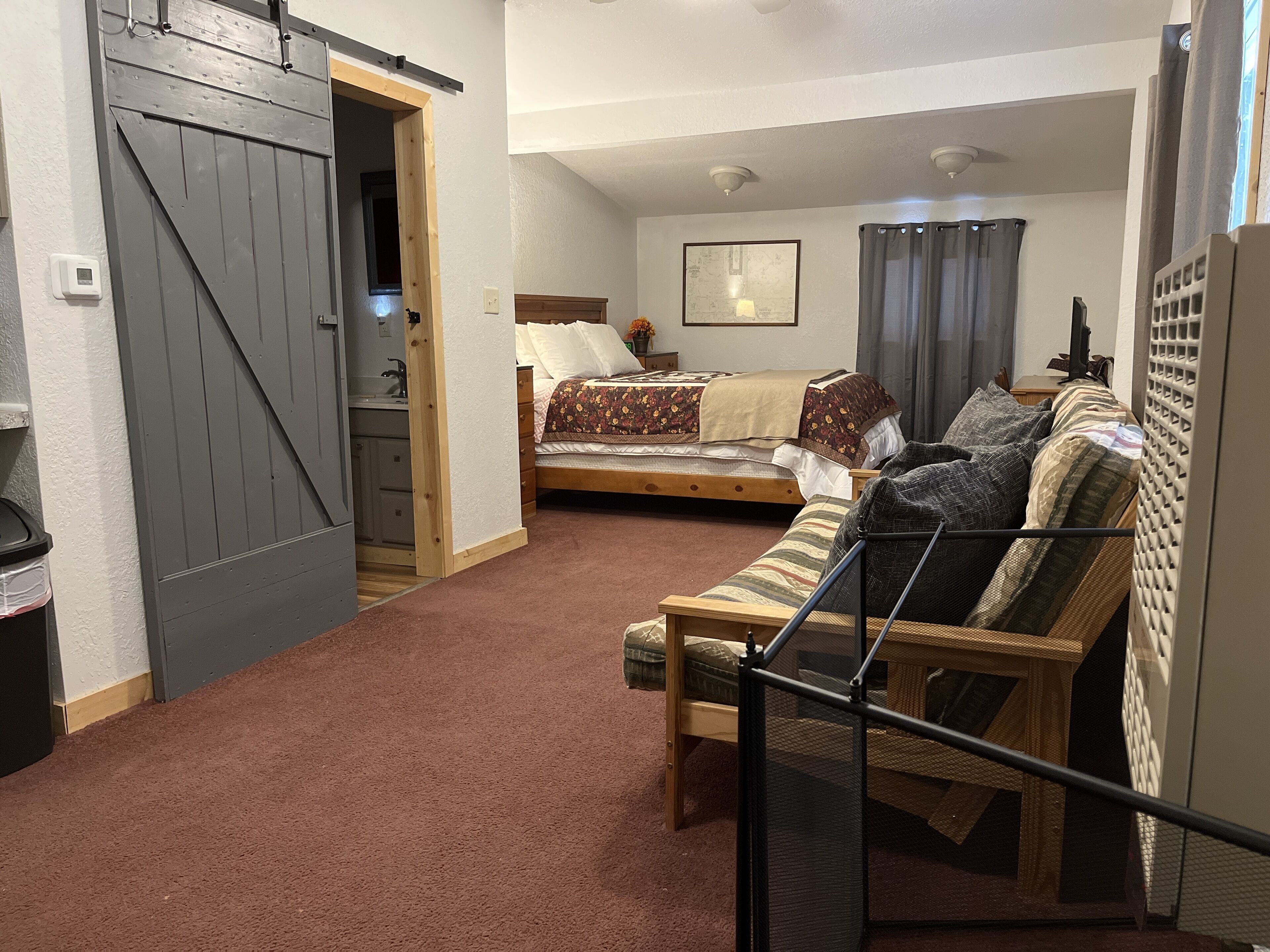 A bedroom with a bed, a sofa, a wooden door, and a small kitchenette.
