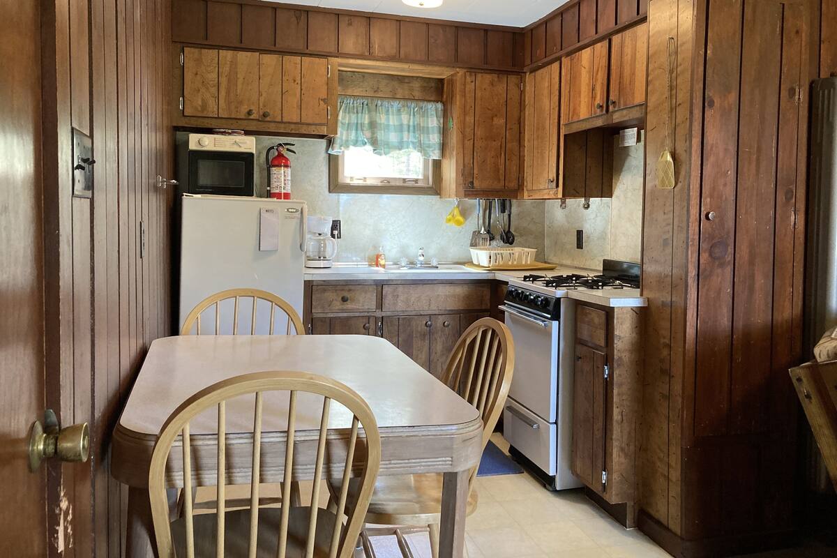 Eine Küche mit Holzausstattung, einem Kühlschrank, einem Herd und einem Esstisch mit Stühlen.