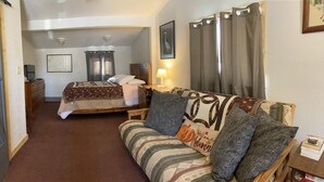A hotel room with a bed, a sofa, a desk, and a lamp. - Musky Joes Twin Pines Resort (Hayward)