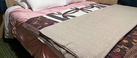 Una cama bien hecha con colcha rosa y beige, almohadas blancas y una manta estampada con motivos florales.