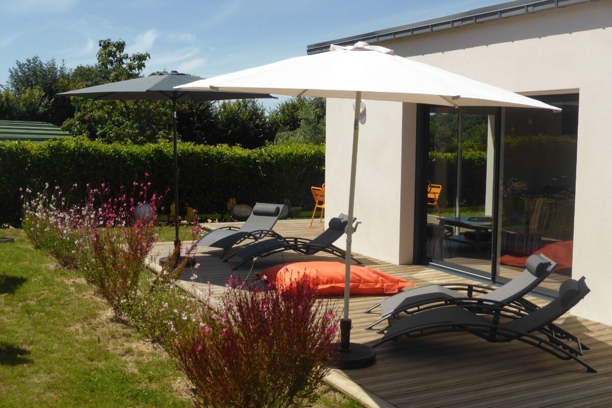 Une terrasse extérieure avec des chaises longues et des parasols, une terrasse en bois et une porte vitrée donnant sur un espace de patio.