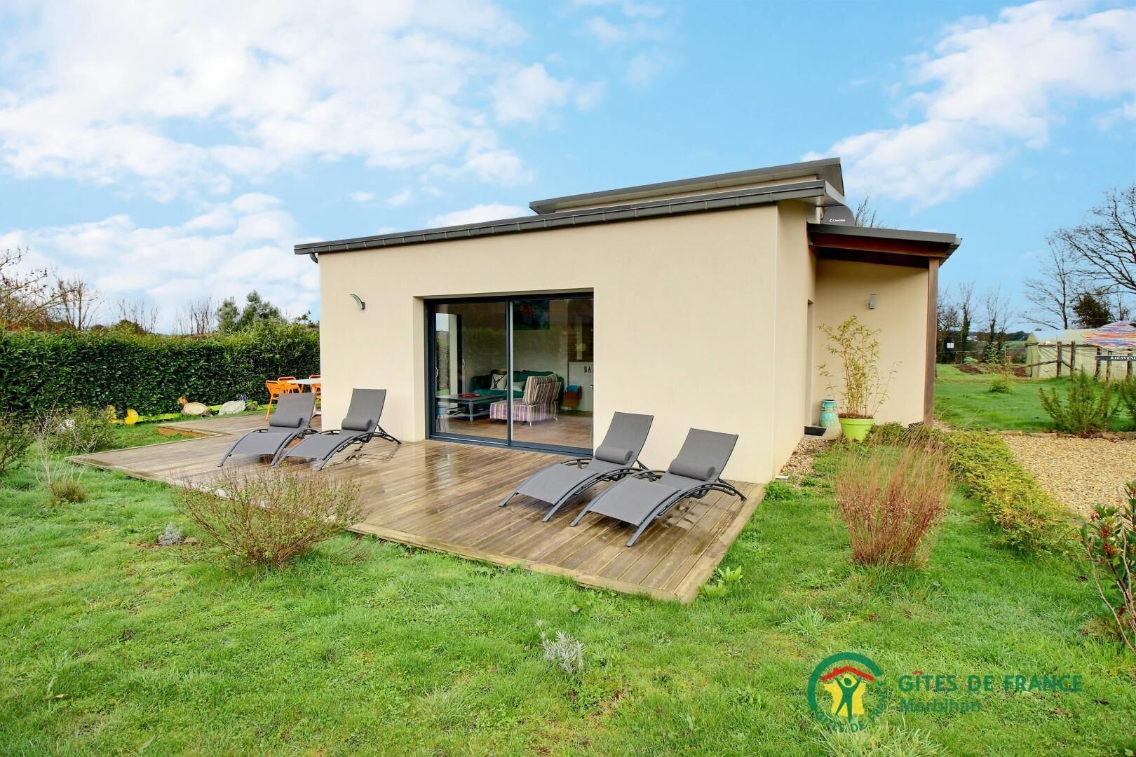 Een modern huis met een terras, zitplaatsen buiten en een tuin.