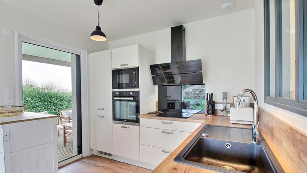 A modern kitchen with white cabinets, a black range hood, and a wooden countertop. - Le Grand Chemin - Ferel (FEREL)