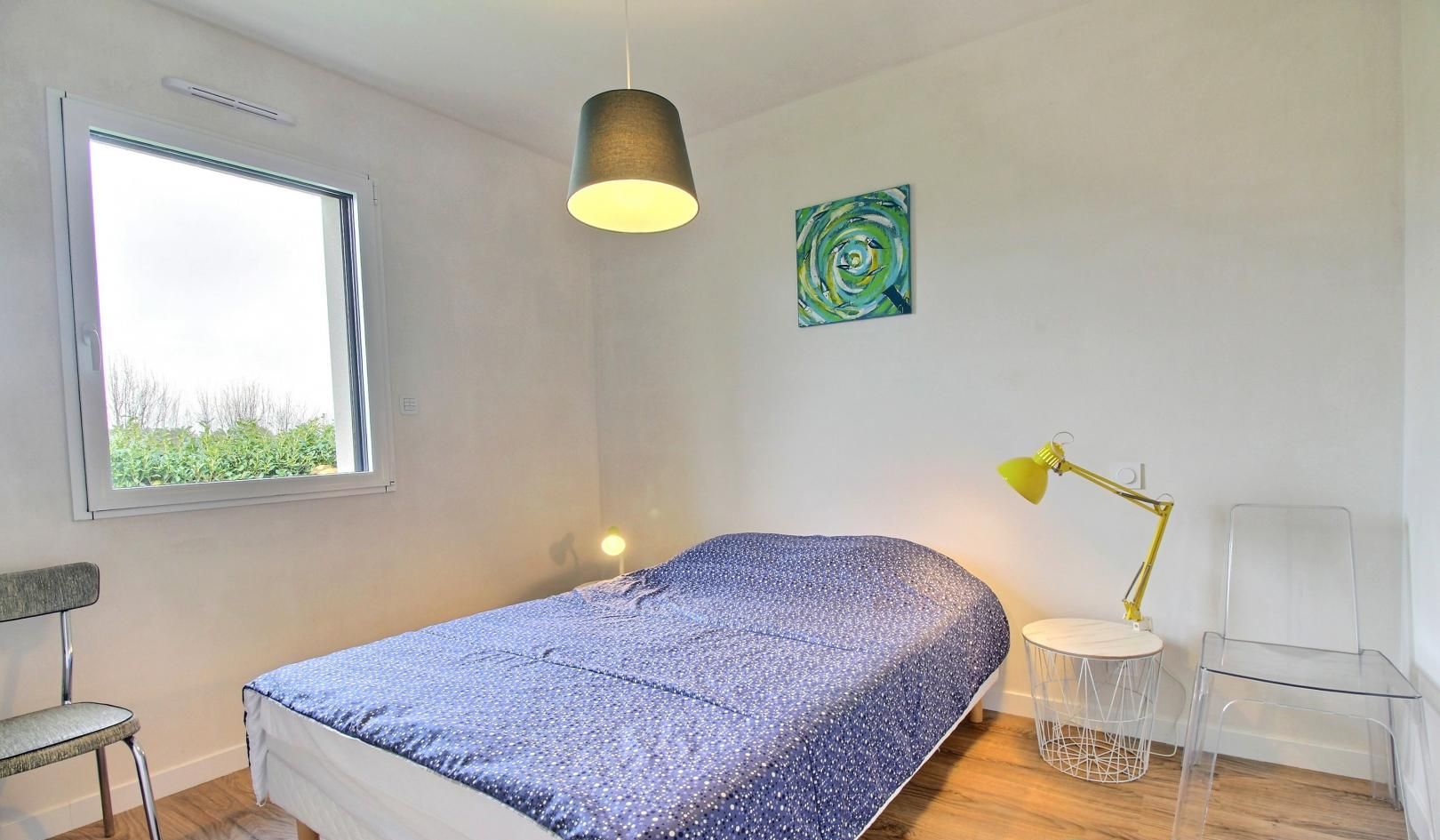 A bedroom with a bed, a desk, a chair, a window, a lamp, and a painting.
