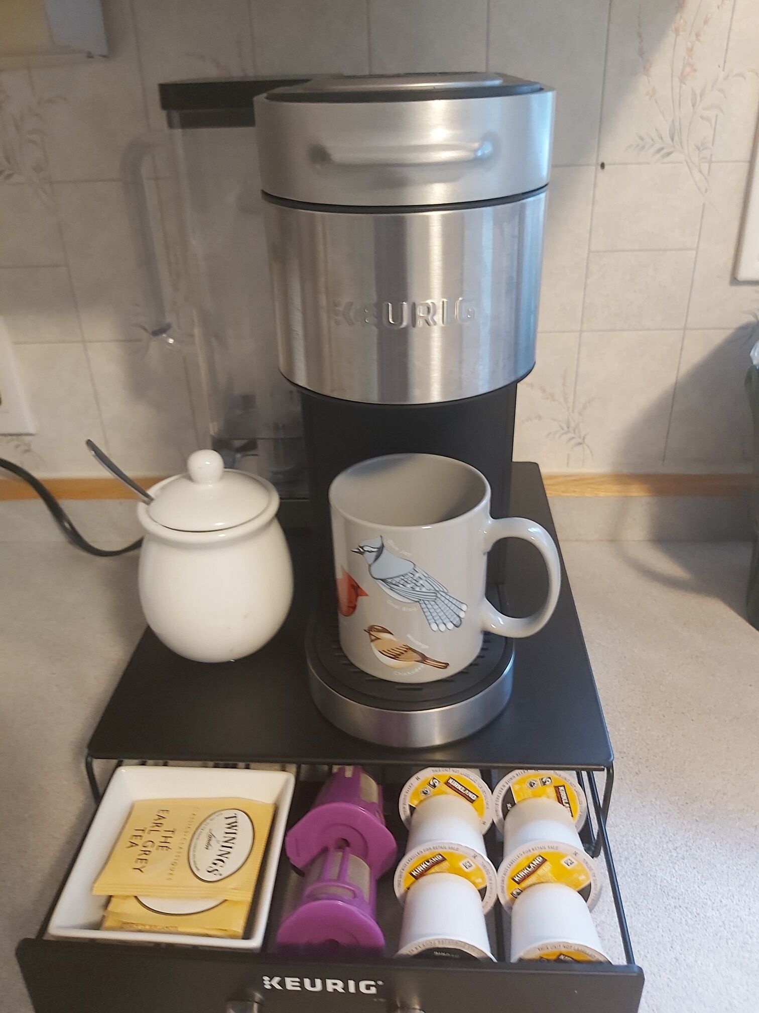 Une machine à café Keurig, avec une tasse et une cafetière, posées sur un support noir.