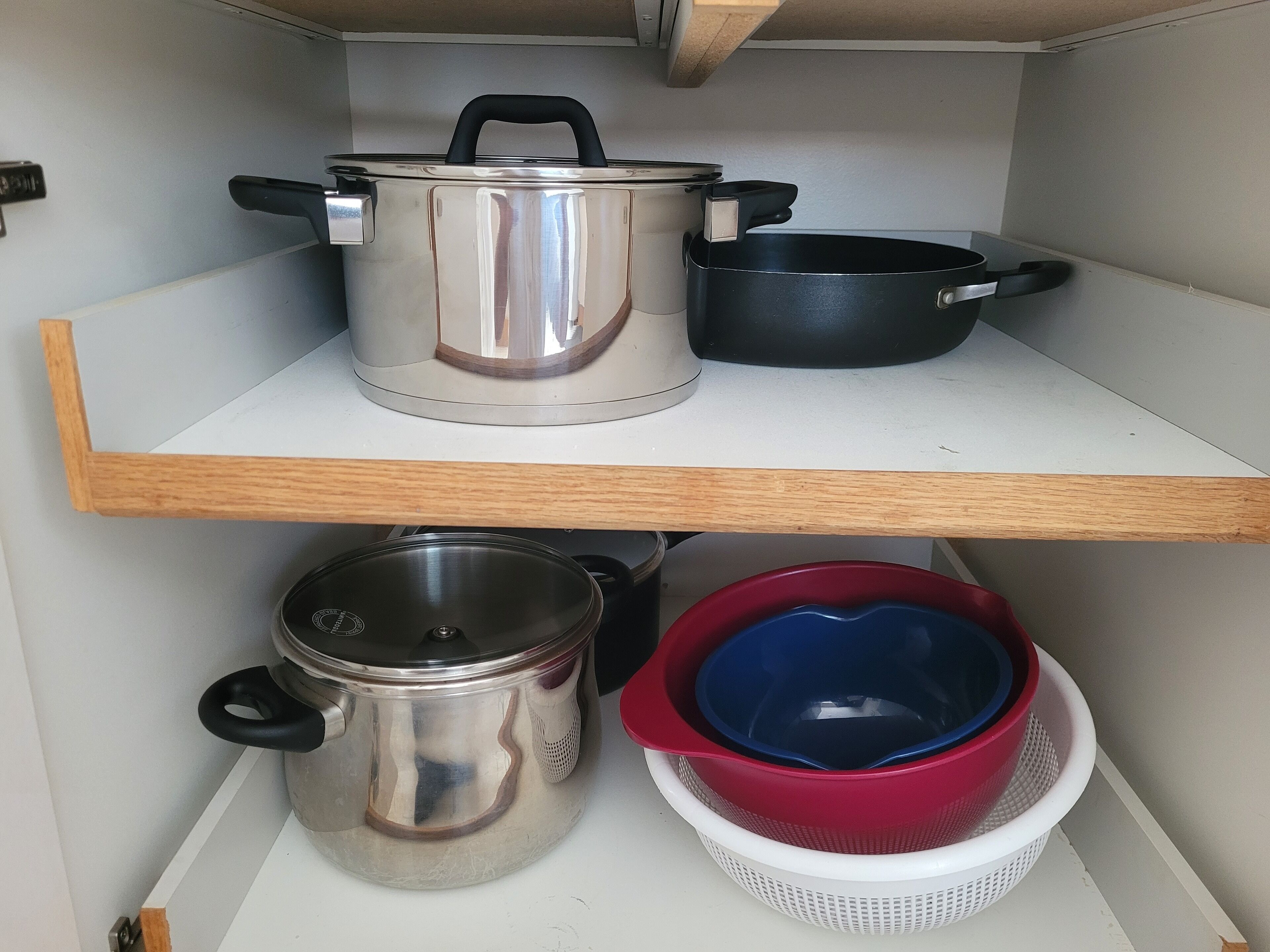 A kitchen shelf with stainless steel cookware, including a pot, pan, and a large pot with a lid.