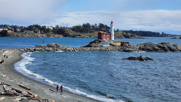 A coastal scene with a lighthouse, rocky shoreline, and a small building.