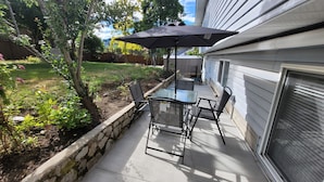 A patio with a table and chairs, a large umbrella, and a stone planter.