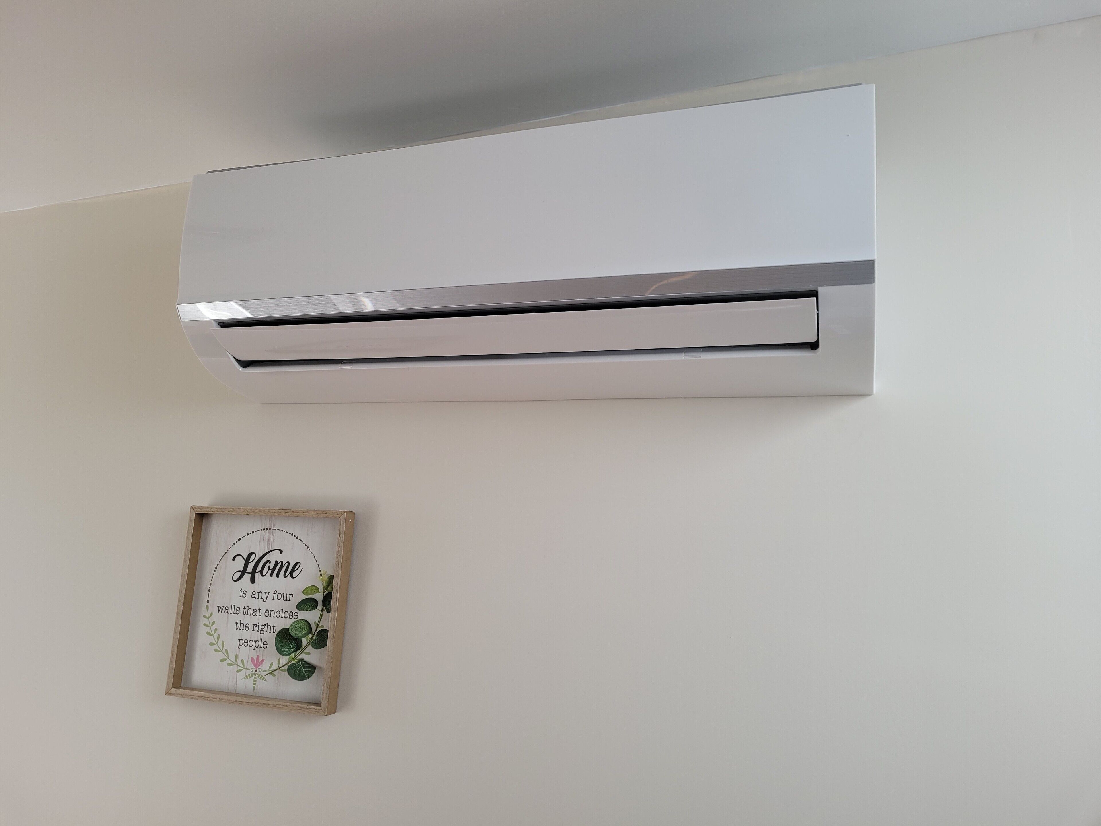 A wall-mounted air conditioner with a framed quote below it.