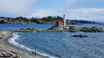 A coastal scene with a lighthouse, rocky shoreline, and a small building.