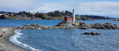 Un paysage côtier avec un phare, une côte rocheuse et un petit bâtiment.