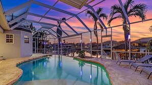 A pool area with a clear view of the pool, lounge chairs, and a covered structure with a view of the sunset. - Villa Encore (Cape Coral)