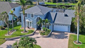 A large, single-story house with a grey roof and blue exterior walls, surrounded by a well-maintained lawn and palm trees. - Villa Encore (Cape Coral)