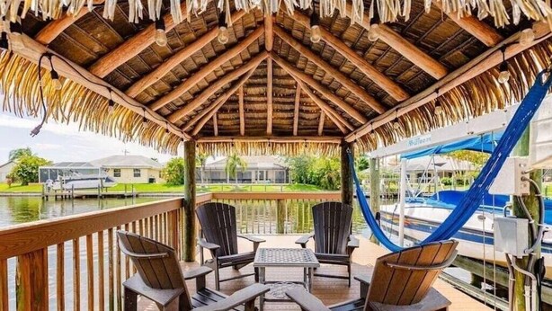 A wooden deck with a thatched roof, overlooking a body of water and a marina. - Villa Encore (Cape Coral)