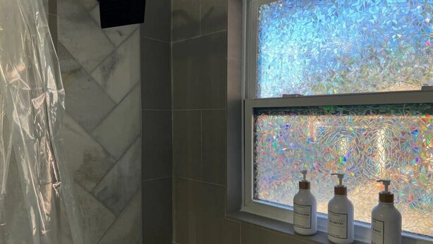 Kylpyhuoneessa on himmeälasinen ikkuna, suihkutila ja ikkunalaudalla kolme pulloa hygieniatuotteita.