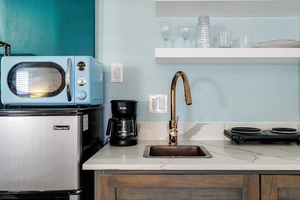 A kitchen with a stainless steel refrigerator, a blue microwave, a coffee maker, a gold faucet, and a marble countertop.