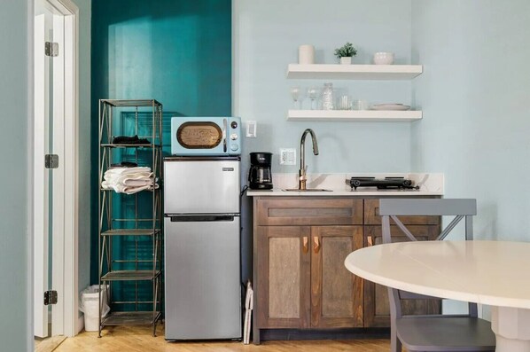 A compact kitchen with a refrigerator, microwave, coffee maker, and a small dining table.