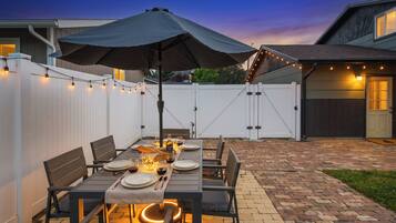 An outdoor patio with a table set for dining, surrounded by chairs and an umbrella.